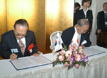 協定書にサインをする金会長と岩永町長